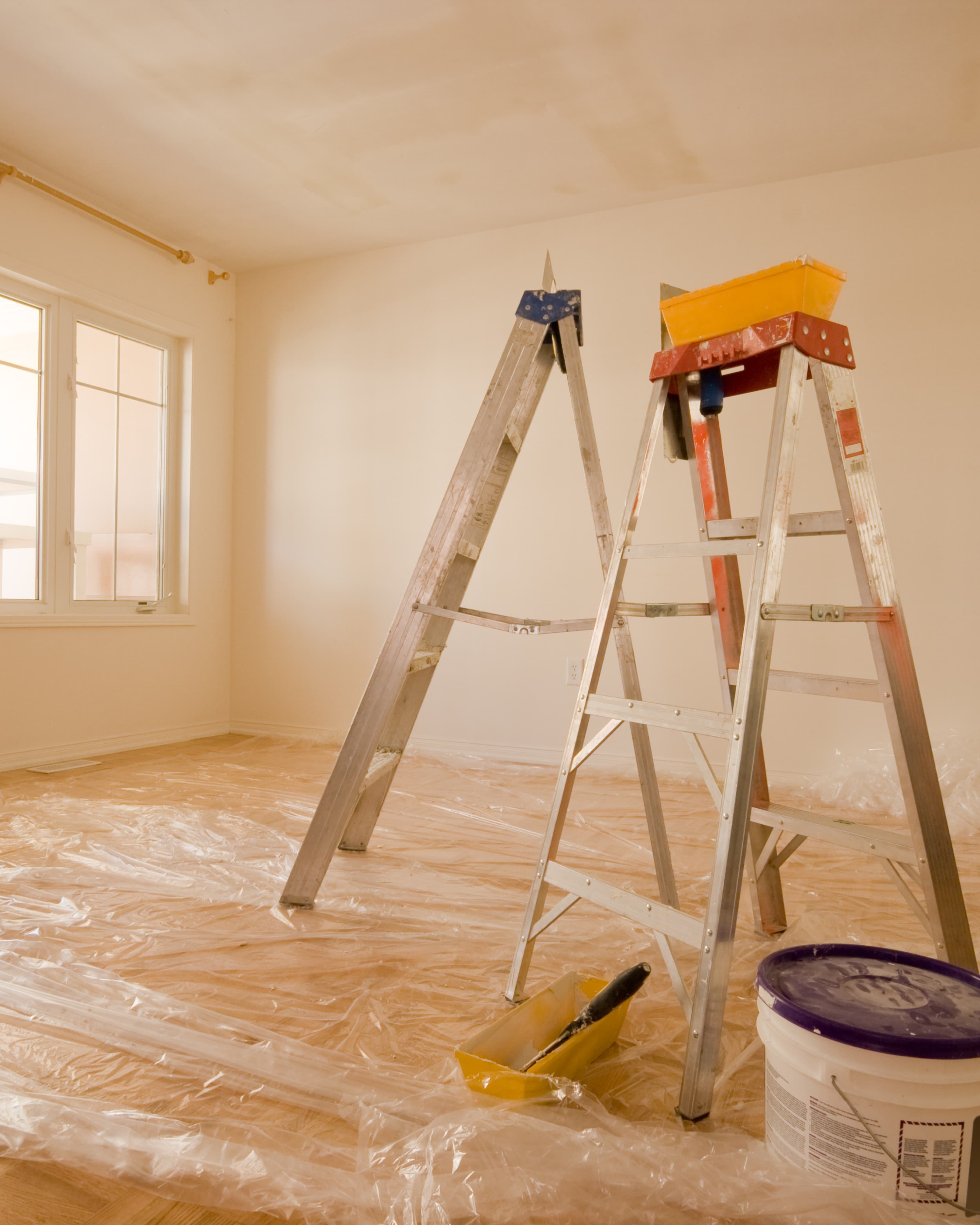 Empty residential room being prepped for repaint with ladder and drop cloths